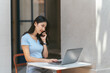 © PaeGAG - Portrait of beautiful Asian woman sitting outdoors at coffee shop restaurant during summer, using smart wireless technology computer laptop and smartphone, relaxing coffee break at cafe restaurant.