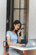 © PaeGAG - Portrait of beautiful Asian woman sitting outdoors at coffee shop restaurant during summer, using smart wireless technology computer laptop and smartphone, relaxing coffee break at cafe restaurant.