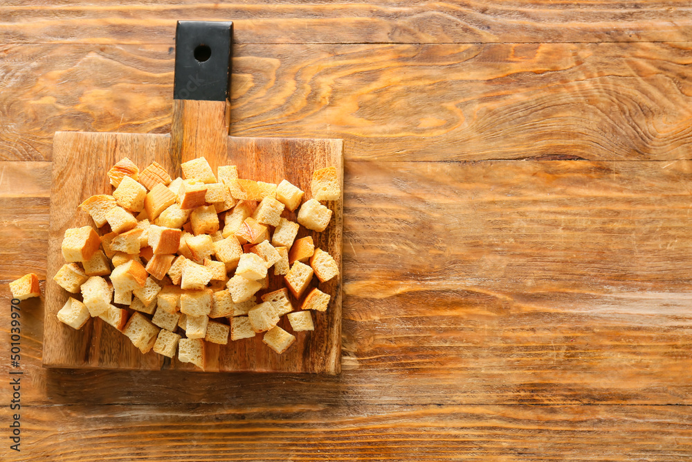 Chopping board with tasty croutons on wooden background