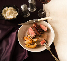 Sliced Steak And Onions In A Plate; Piece Of Steak Pierced On A Fork; Side Of Mashed Potatoes And Red Wine