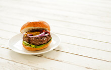 A Hamburger On A White Plate On A White Picnic Table