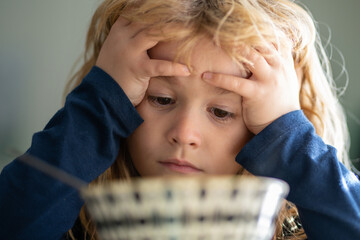 Portrait of sad child having breakfast at home. Portrait of sweet little kid boy with blonde hair eating soup from plate holding spoon, closeup kids face.