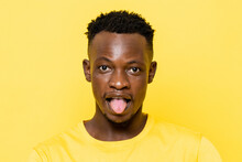 African Man Sticking His Tongue Out On Yellow Color Background In Light Studio