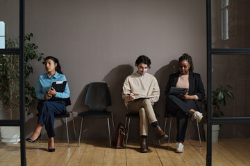 Young job candidates sitting on chairs in waiting room and filling forms before interview