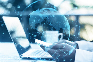 Aufkleber - Close up of hands using laptop and smartphone on desktop with coffee cup, glowing polygonal globe and social icons on blurry outdoor background. Connect and data concept. Double exposure.