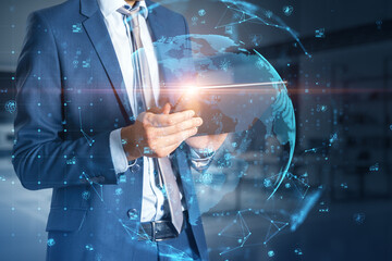 Poster - Close up of businessman hand holding tablet with glowing polygonal globe with social icons on blurry office interior background. Connect and data concept. Double exposure.