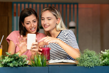 Wall Mural - Portrait of two beautiful women having fun, using phone together and chatting in cafe