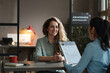 © AnnaStills - Young woman sitting at table and smiling while manager examining her resume during job interview