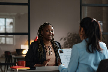 African young woman talking about her work experience to interviewer while they sitting at table during job interview