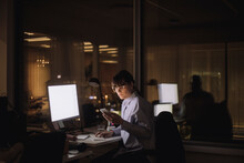 Businesswoman Text Messaging On Mobile Phone Sitting In Office At Night