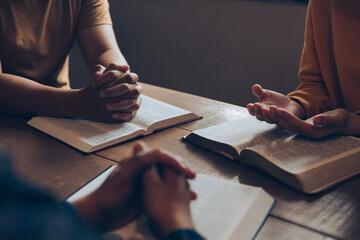 Christians and Bible study concept.Christian family sitting around a wooden table with open bible page and holding each other's hand praying together.