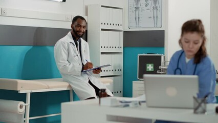 Wall Mural - Portrait of general practitioner with checkup files in cabinet waiting to start medical appointment. Male physician and health care assistant working together in office to help people.