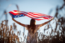 Up Shot Of A Young Girl With Waving Flag Against Setting Sun. Girl Holding Flag Of USA