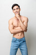 © Atstock Productions - Smiling handsome muscular Asian man with black hair and naked torso touching chin while standing on gray isolated background in light studio