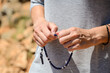 © Ajdin Kamber - Hands of pilgrim holding the rosary. Christian woman praying in front of cathedral. Woman with hands crossed.