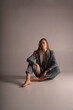 © evgenzz - A beautiful blonde girl in a pantsuit with an unbuttoned jacket from under which a beautiful slender sexy body and underwear can be seen posing on a white background sitting on the floor barefooted