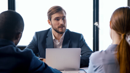 Poster - Young man in a suit talking with colleagues at meeting