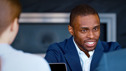 Poster - Young afro american man in a suit talking with colleagues in coworking