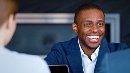 Poster - Smiling afro american businessman in suit talking with colleagues at table