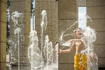 Wall Mural - Boy having fun in water fountains. Child playing with a city fountain on hot summer day. Happy kids having fun in fountain. Summer weather. Active leisure, lifestyle and vacation