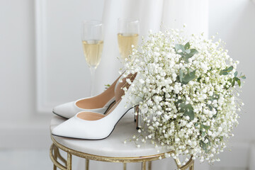 Wedding decor with bride's white shoes, flower bouquet, rings, glasses of champaign on the table