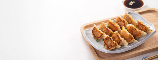 Pan-fried gyoza dumpling jiaozi in a plate with soy sauce on white table background.