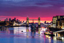 Tower Bridge And HMS Belfast Reflecting In A Still River Thames At Sunset, London