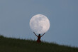 © robertharding - Full moon portrait at blue hour with a girl holding the moon above her head, Emilia Romagna