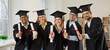 © Studio Romantic - Happy students at graduation event. Joyful mixed race multiethnic male and female college or university graduates in hats and robes standing in classroom, showing diploma scrolls and smiling at camera