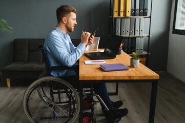 Wall Mural - Disabled person in the wheelchair works in the office at the computer. He is smiling and passionate about the workflow.