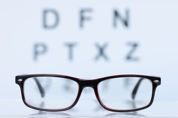 Wall Mural - Glasses in black frame lying on background of eye test table closeup