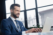 © LIGHTFIELD STUDIOS - joyful economist typing on laptop on blurred foreground in office.
