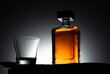 Empty glass and bottle of whiskey on black background and backlight