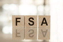 FSA - An Abbreviation Of Wooden Blocks With Letters On A White Background. Reflection Of The Caption On The Mirrored Surface Of The Table. Selective Focus. Fsa - Shortt For Flexible Spending Account