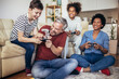 © Mediteraneo - Smiling family enjoying time together at home sitting on sofa in living room and playing video games.