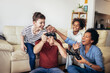 © Mediteraneo - Smiling family enjoying time together at home sitting on sofa in living room and playing video games.