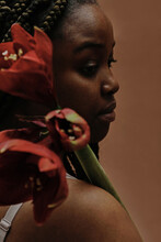 African Girl Looking Through Her Shoulder Holding Big Red Flower Isolated On Brown Background