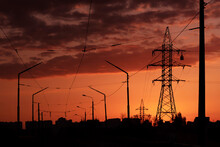 .black Silhouettes Of Power Line Pylons, Poles, Wires And Houses At Sunset