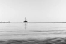 .black And White Photo Of The Silhouette Of A Sailing Single-masted Yacht, Leaving The Sea From The Coast In Calm