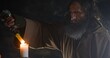 © procinemastock - Aged hermit igniting candle in cave