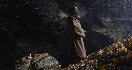 Wall Mural - hermit man with robe in the entrance of a old cave in front of a valley