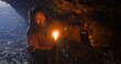 © procinemastock - Old druid walks carefully in dark ancient cave with candle
