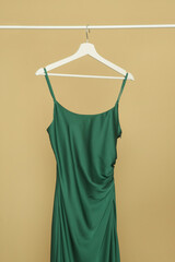 Elegant pine green silk camisole long dress hanging on clothing rack against beige background
