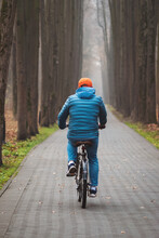 Man Rides Bicycle On Autumn Weekend In Dull Foggy Park, Rear View