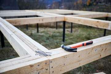 Hammer and nails laying on wooden pile foundation for future frame house. Constuction site and work instrument concept.