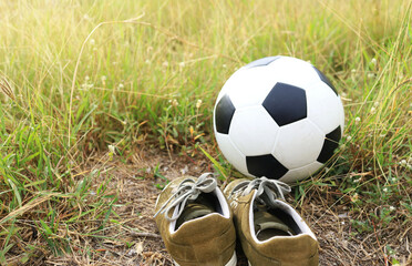 A soccer ball or football and shoes on a long grass field in the countryside at dawn morning light.