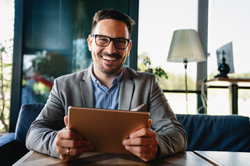 Portrait of young successful businessman with digital device working in corporate business office