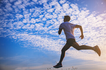 Wall Mural - Silhouette of young man running sprinting on road. Fit runner fitness runner during outdoor workout with blue sky as background.