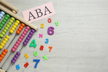 Paper Sheet With Abbreviation ABA (Applied Behavior Analysis), Abacus And Colorful Numbers On White Wooden Table, Flat Lay. Space For Text