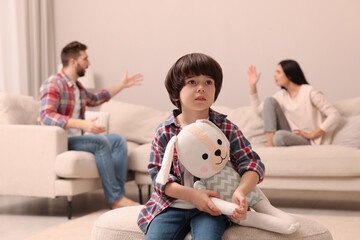 Wall Mural - Sad little boy with toy and his arguing parents on sofa in living room